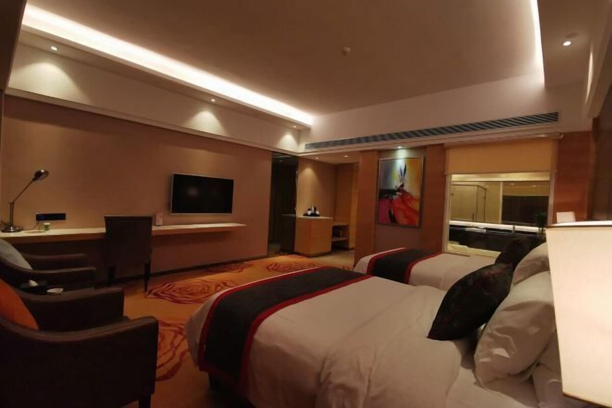 A hotel room with a bed, a desk, a chair, a TV, and a painting on the wall.
