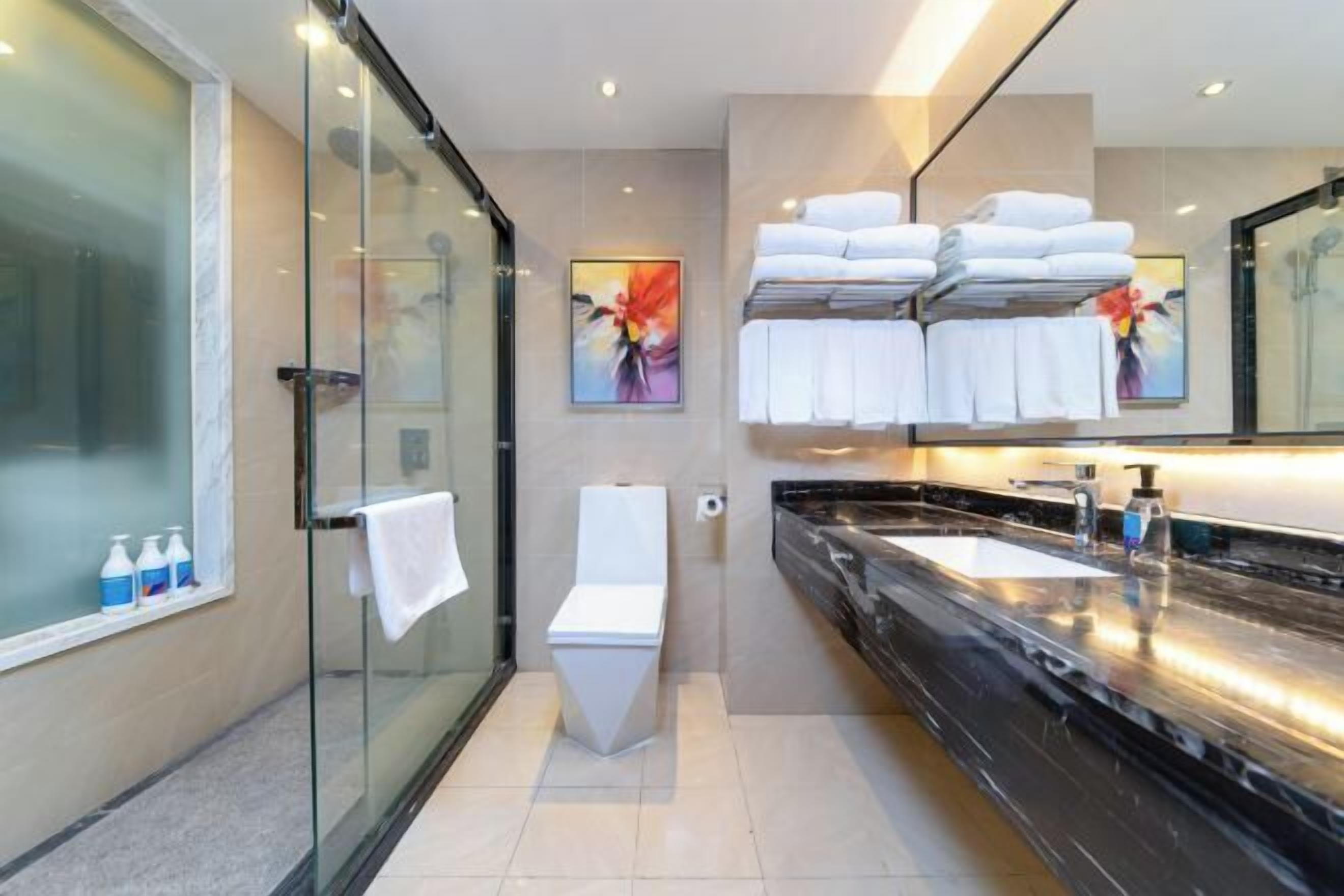 Un baño moderno con cabina de ducha de vidrio, un inodoro, un lavamanos grande con encimera negra y un perchero con toallas dobladas.