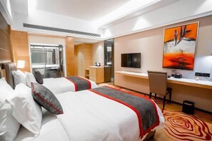 A hotel room with two beds, a desk, a chair, a TV, and a painting on the wall. - Perthden (Hanging) Gardens Hotel (Shenzhen)