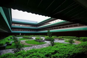 A multi-level building with a central courtyard featuring pathways, greenery, and a water feature.