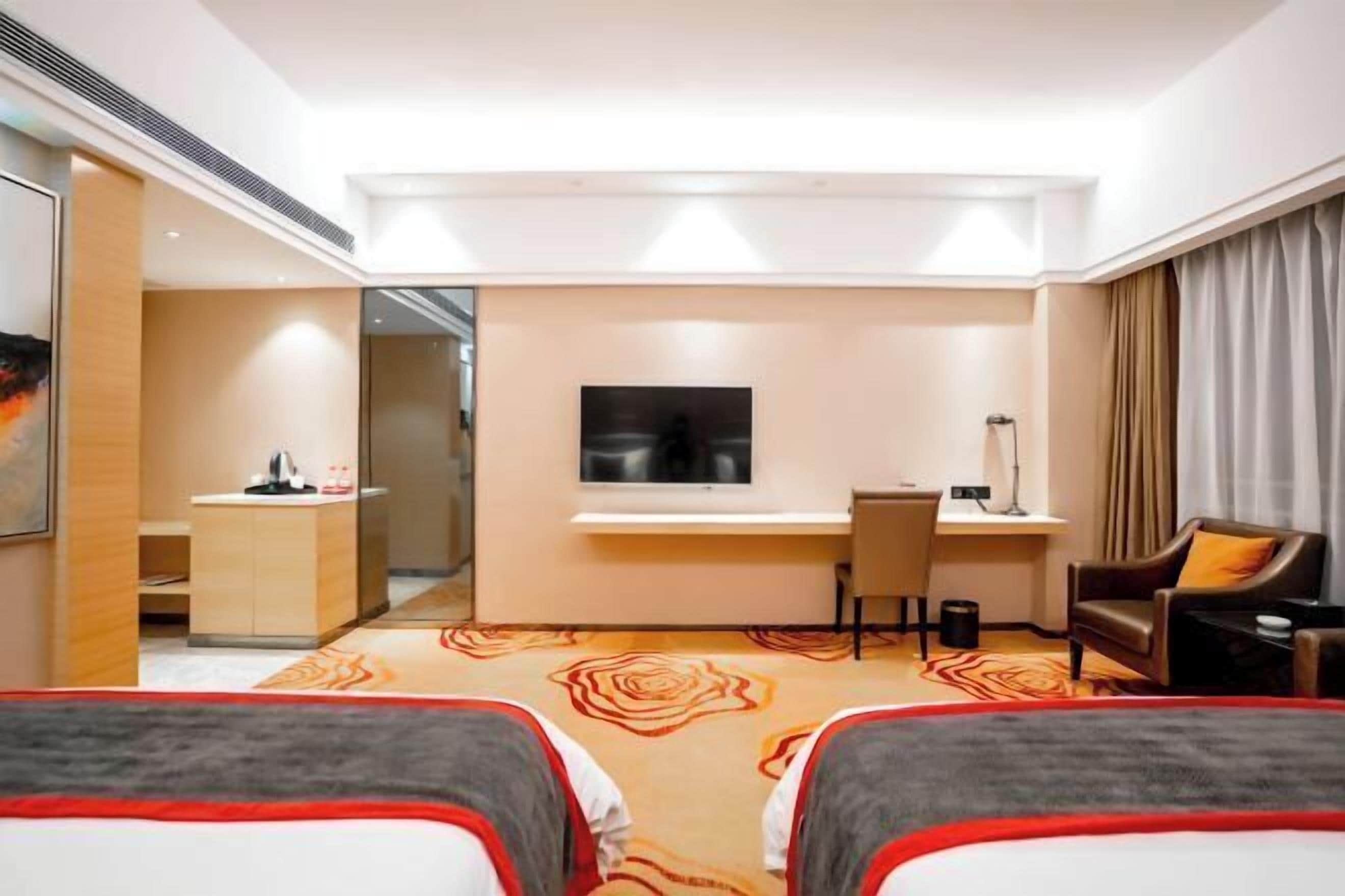A hotel room with two beds, a desk, a television, and a seating area.