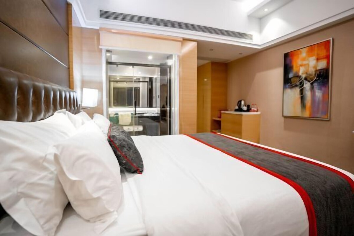 A hotel room with a large bed, a desk, and a painting on the wall.