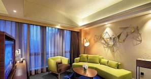 Quarto de hotel moderno com um sofá verde, uma mesinha de centro e um objeto decorativo na parede.