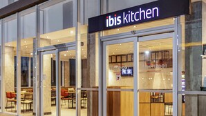Un restaurant moderne avec des portes en verre et une enseigne indiquant « ibis kitchen ».