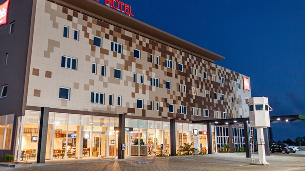 Un hôtel à la façade à carreaux, avec une enseigne «IBIS HOTEL» bien visible et une entrée bien éclairée.