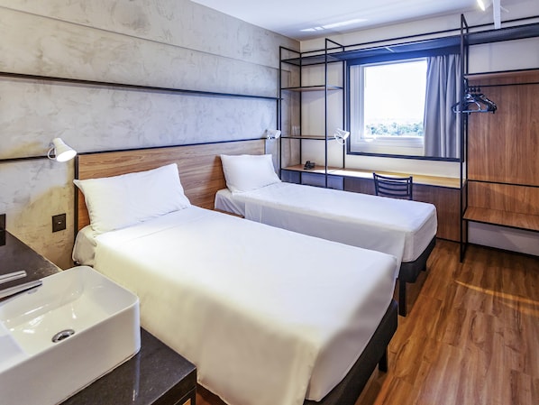 Habitación de hotel con dos camas, un escritorio, una silla, una ventana con cortinas y un armario.