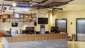 Un comptoir d’accueil moderne doté de deux écrans d’ordinateur, d’un plan de travail en bois et d’un plafond avec des poutres apparentes et des luminaires.