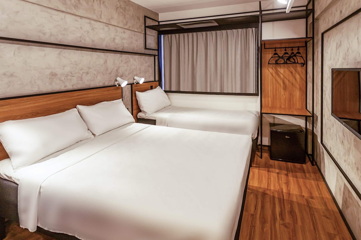 A hotel room with two beds, a wardrobe, a TV, and a window with curtains.
