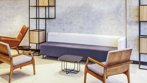 Un espace de détente moderne comprenant un canapé, deux fauteuils en bois, une petite table et un motif géométrique sur le mur.