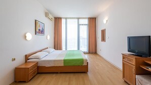 A hotel room with a bed, a TV, a nightstand, and a window with curtains.