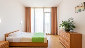 A bedroom with a bed, a dresser, a plant, and a window with curtains.