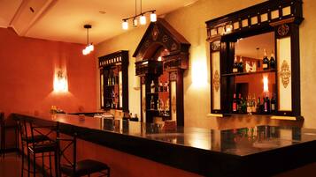 Uma área de bar com um balcão comprido, várias prateleiras com garrafas e algumas cadeiras.