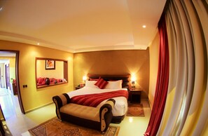 A hotel room with a large bed, a nightstand, a mirror, and a view of the hallway. - Palms Hotel Club (Aarab Sebbah Ziz)