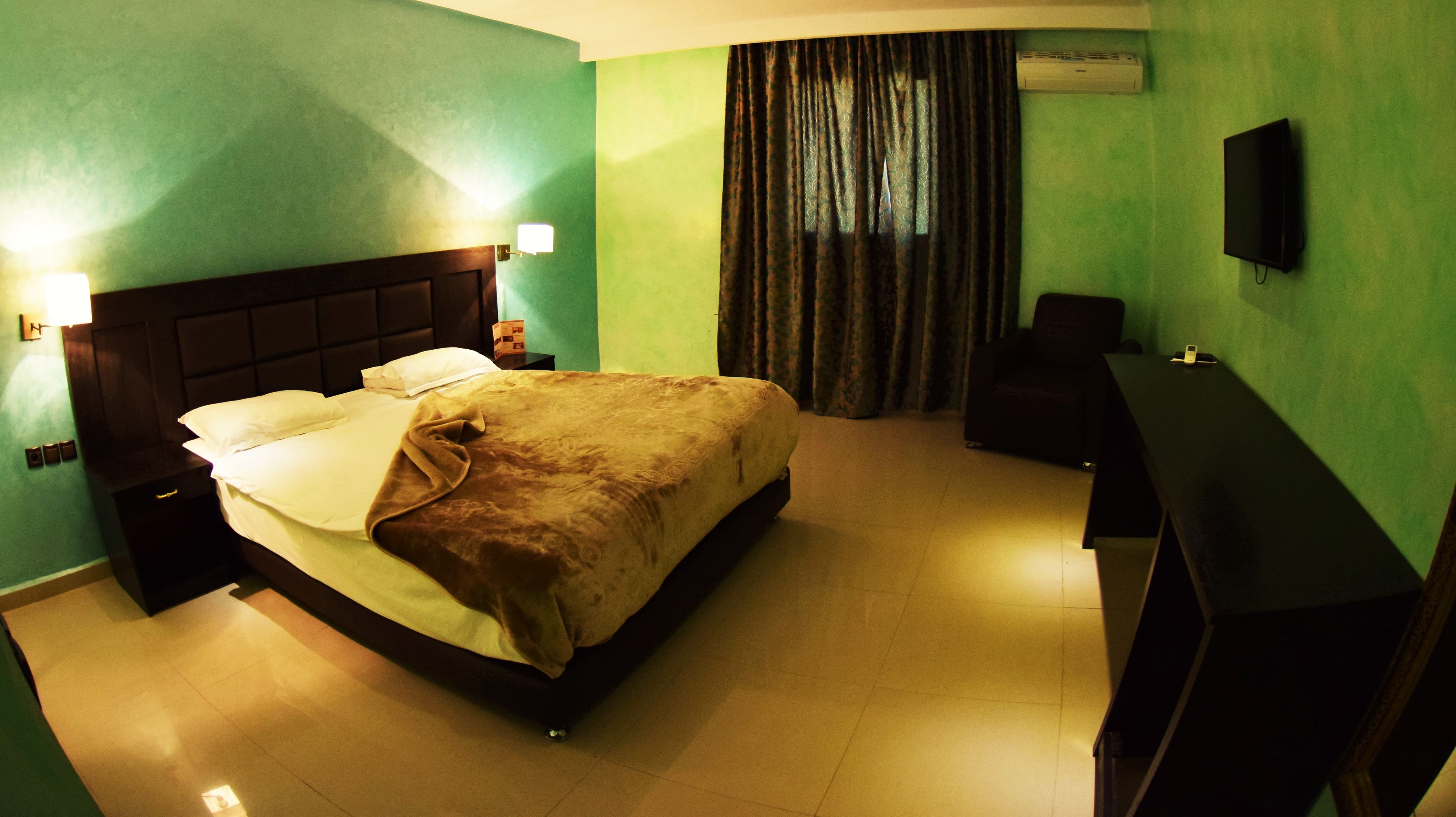 A hotel room with a bed, a desk, a chair, a TV, and a window with curtains.