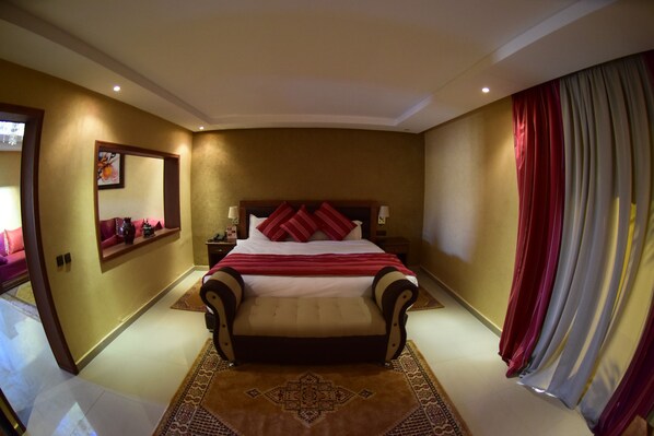 A hotel room with a large bed, a nightstand, a lamp, a mirror, and a window with curtains. - Palms Hotel Club (Aarab Sebbah Ziz)