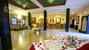 A spacious lobby with a reception desk, seating area, and a decorative table with glasses and a teapot. - Palms Hotel Club (Aarab Sebbah Ziz)