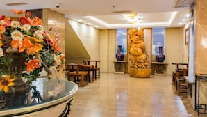 A lobby with a large floral arrangement, a Buddha statue, and a seating area with tables and chairs. - Fudi Hotel (Shanghai)