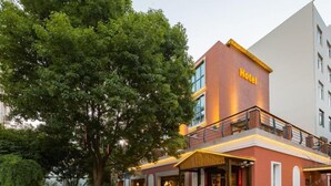 A hotel with a prominent 'Hotel' sign, a covered outdoor seating area, and a large tree in the foreground. - Fudi Hotel (Shanghai)