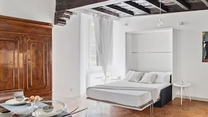 Een moderne slaapkamer met een bed, een klein rond tafeltje en een houten garderobe.