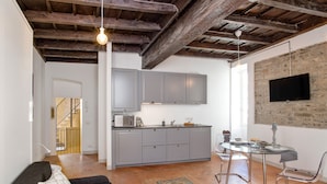 Een moderne keuken met grijze kastjes, een eettafel met stoelen, en een televisie bevestigd aan een stenen muur.