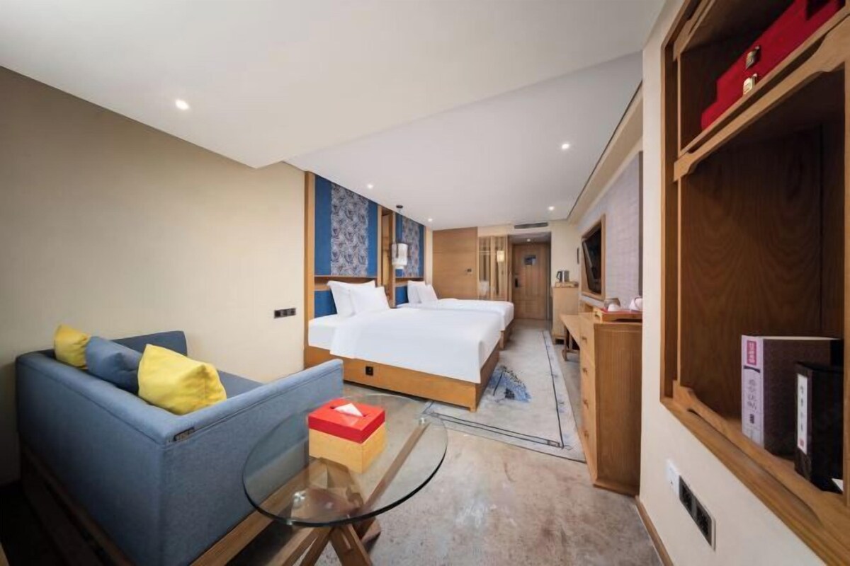 A hotel room with a bed, a sofa, a glass table, and a wooden wardrobe.