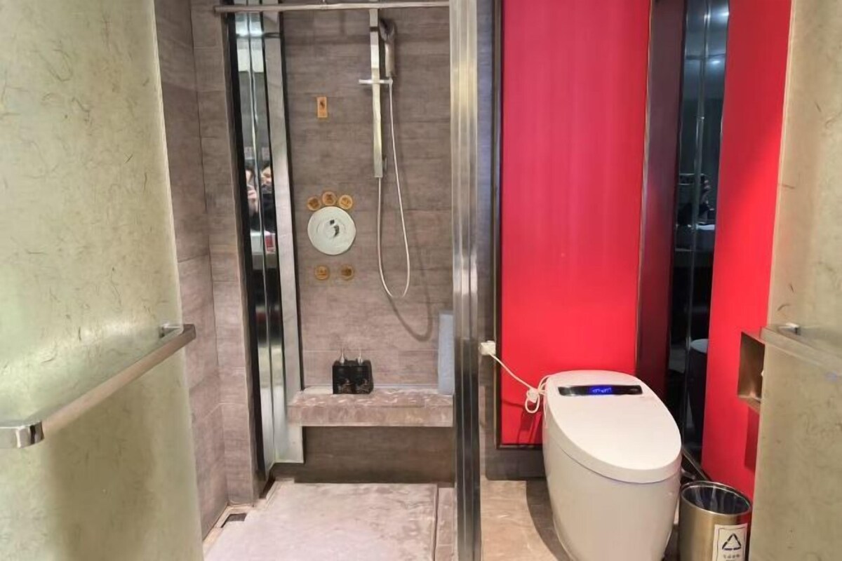 A compact bathroom with a shower, toilet, and a small bench.