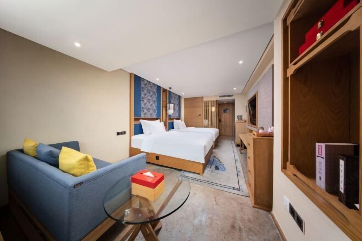 A hotel room with a bed, a sofa, a glass table, and a wooden wardrobe.