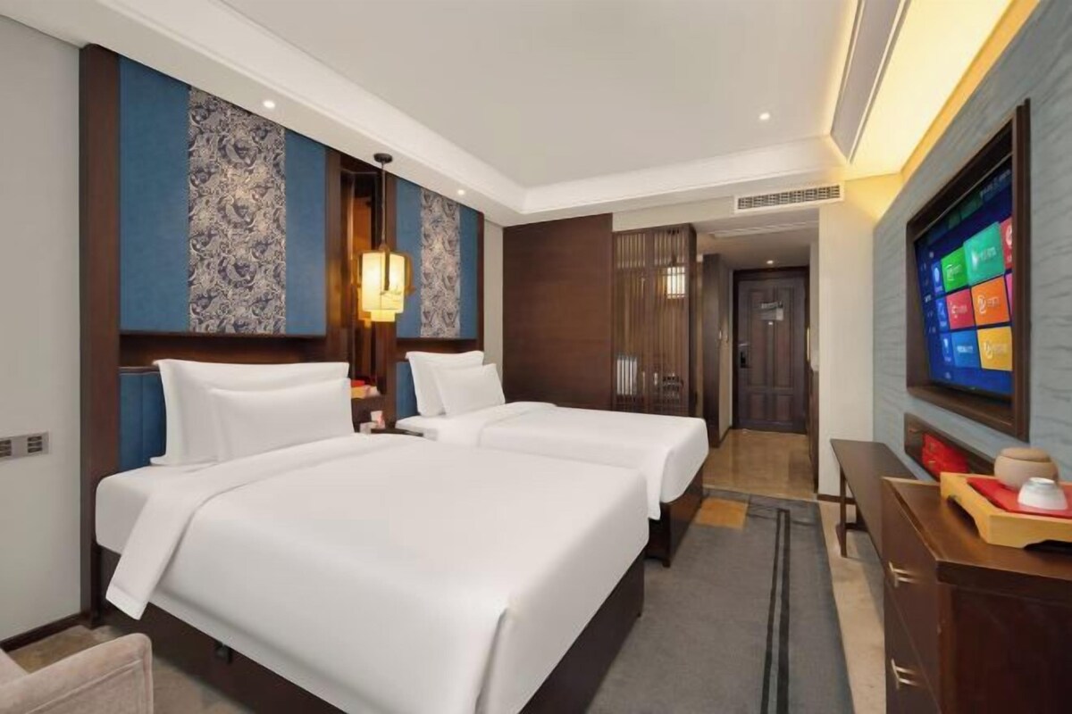 A hotel room with two beds, a TV, and a desk.