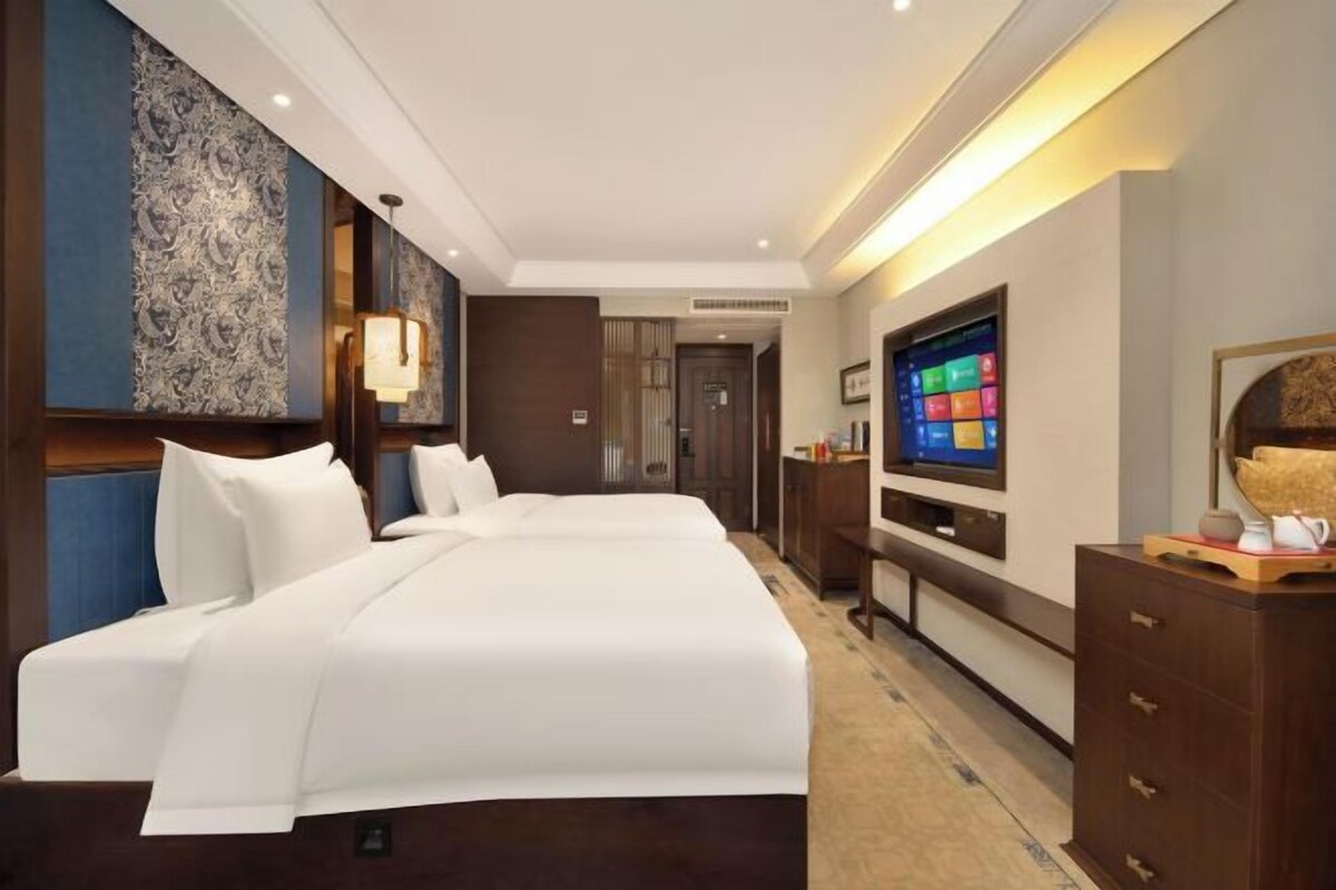 A hotel room with a large bed, a TV, and a wooden dresser.