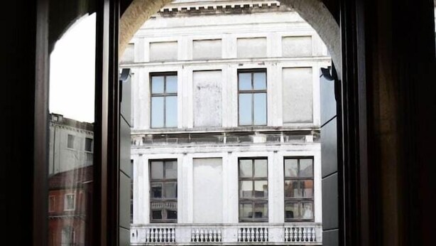 Une vue à travers la fenêtre d’un immeuble doté d’un balcon, avec un cours d’eau et le reflet d’un autre immeuble.
