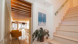 Un intérieur moderne avec un escalier, un couloir doté d’un plafond en bois et un coin salon avec des chaises jaunes.