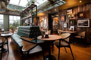 A cozy interior with a green sofa, wooden tables, wicker chairs, and a high ceiling with skylights. - The Angel Inn - The Inn Collection Group (Windermere)