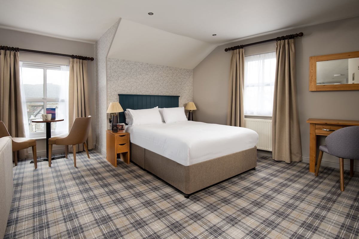 A hotel room with a large bed, a desk, a chair, and a view of the outdoors.