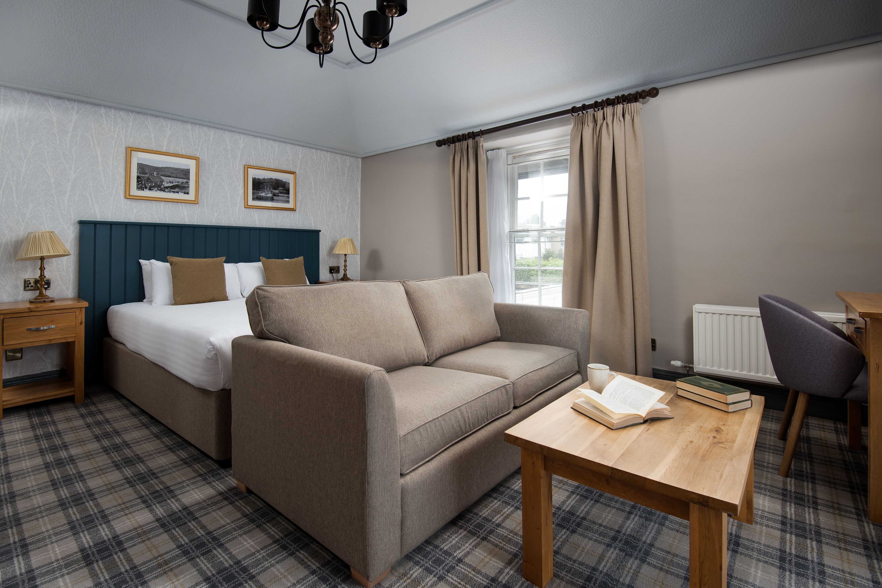 A room with a bed, a sofa, a table with a book, and a lamp.