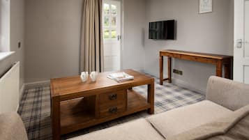 A room with a plaid carpet, a wooden coffee table with two drawers, a beige sofa, a wooden side table, and a television mounted on the wall.