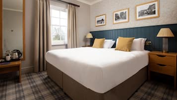 A hotel room with a large bed, a wooden nightstand, a bedside table with a lamp, and a window with curtains. There are three framed pictures on the wall above the bed.