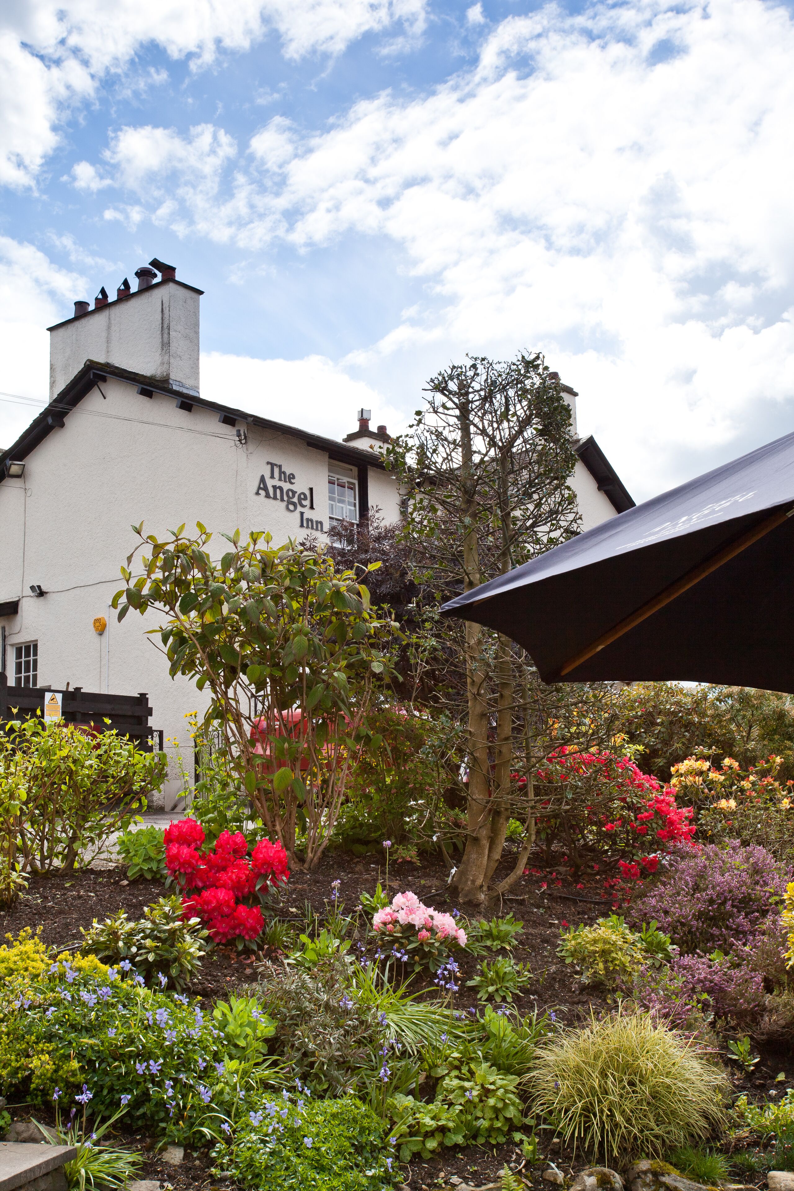 A building labeled "The Angel Inn" with a garden in front featuring various plants and flowers.
