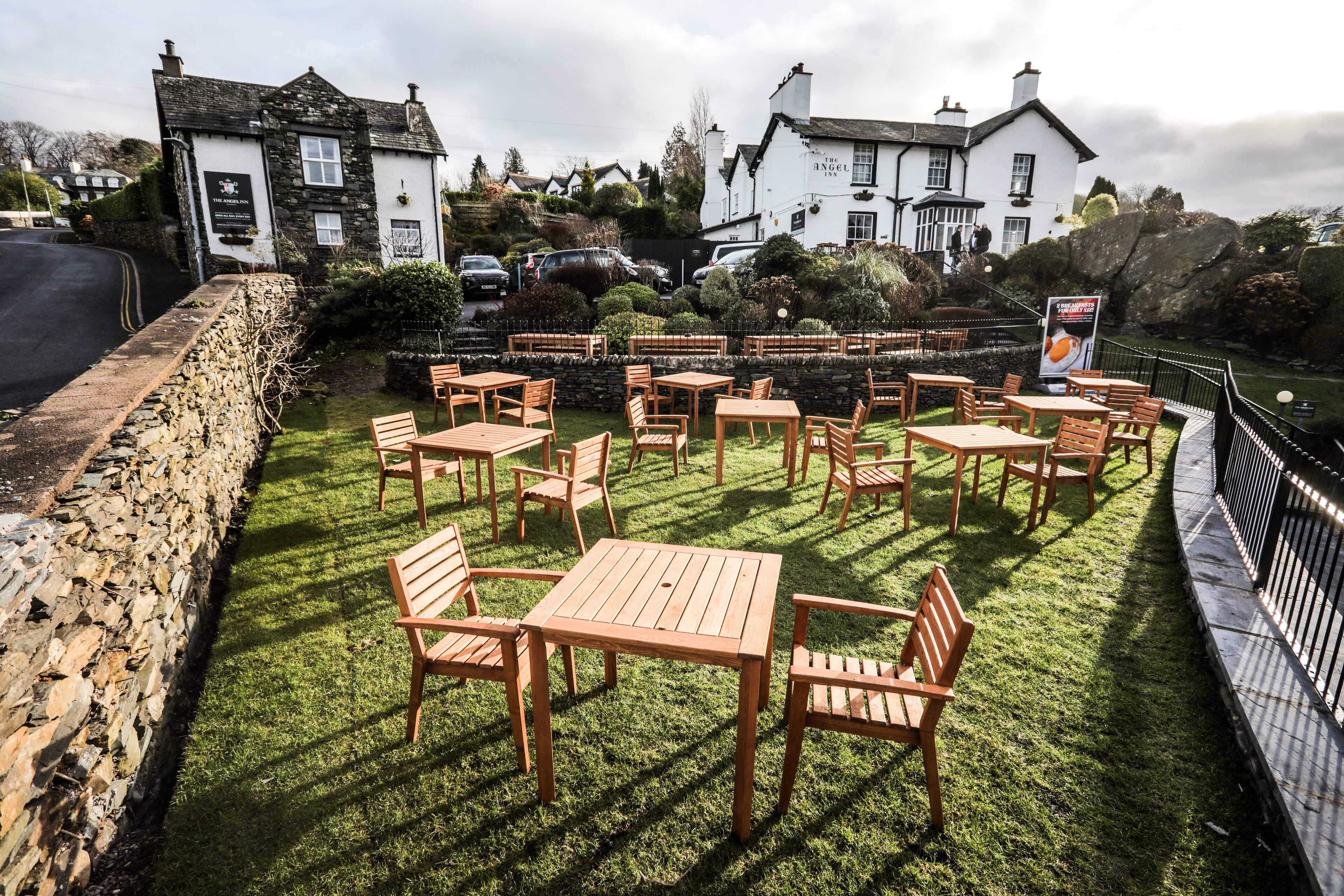 An outdoor seating area with tables and chairs, surrounded by stone walls and a stone pathway.