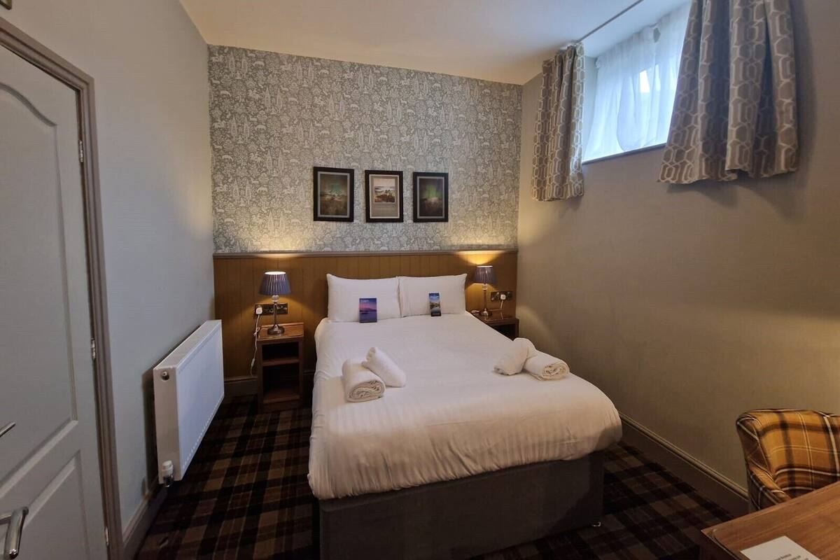 A hotel room with a bed, two bedside tables, a window with curtains, and a wall with three framed pictures.