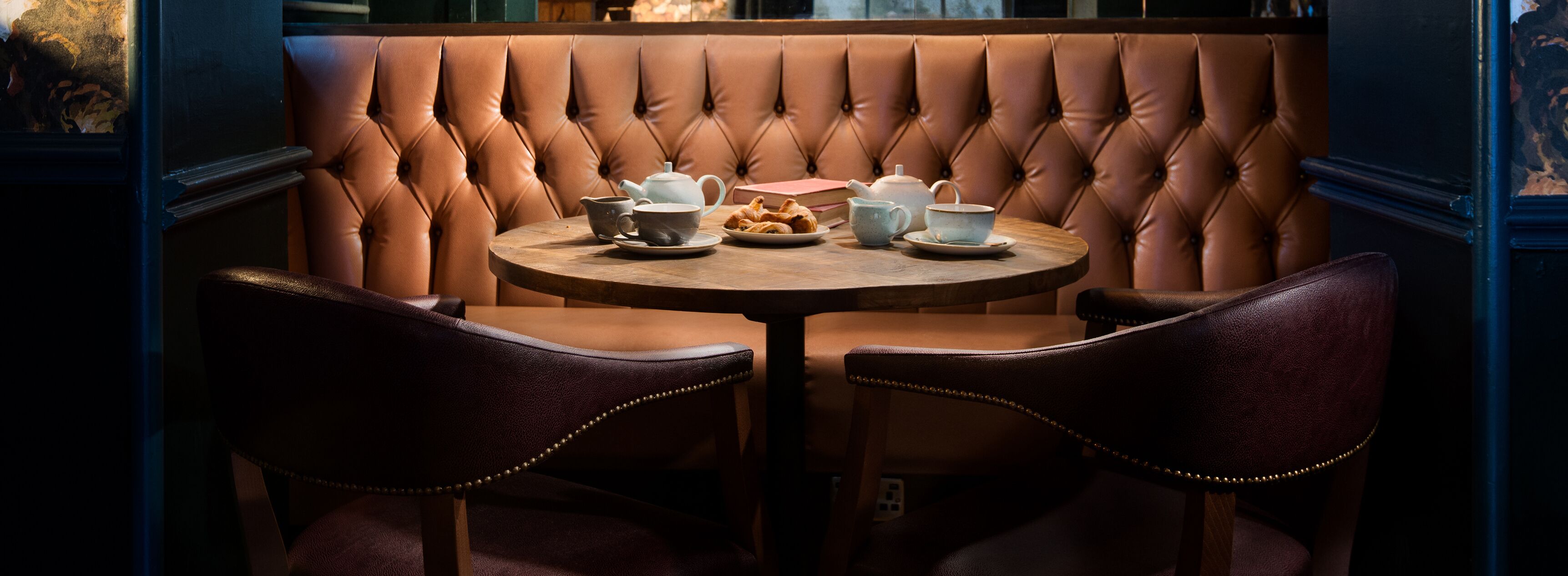A booth with a tufted backrest, two chairs, a round table, and a small book.