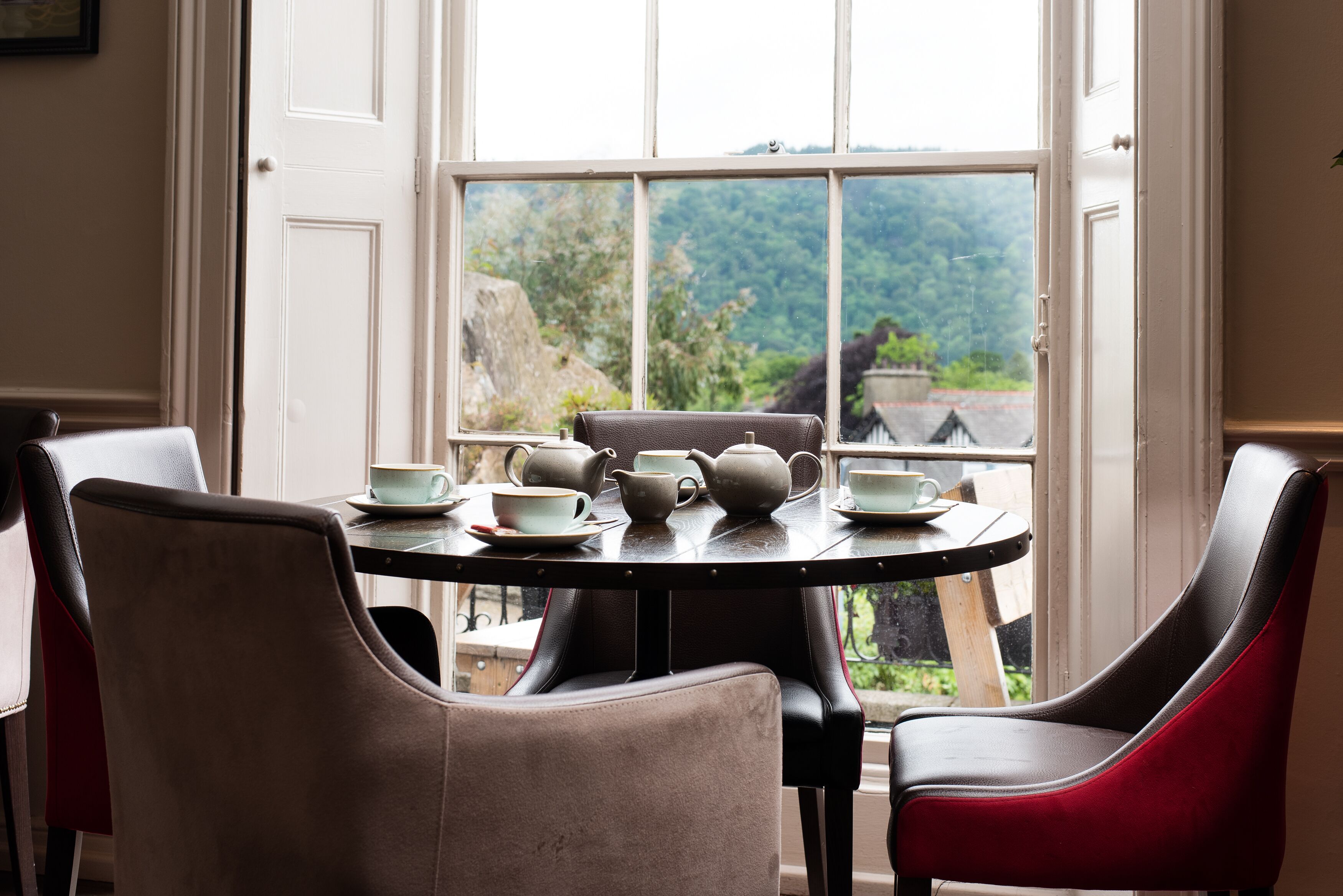 Un coin repas avec une table dressée pour le thé, deux chaises et une vue sur la verdure par la fenêtre.