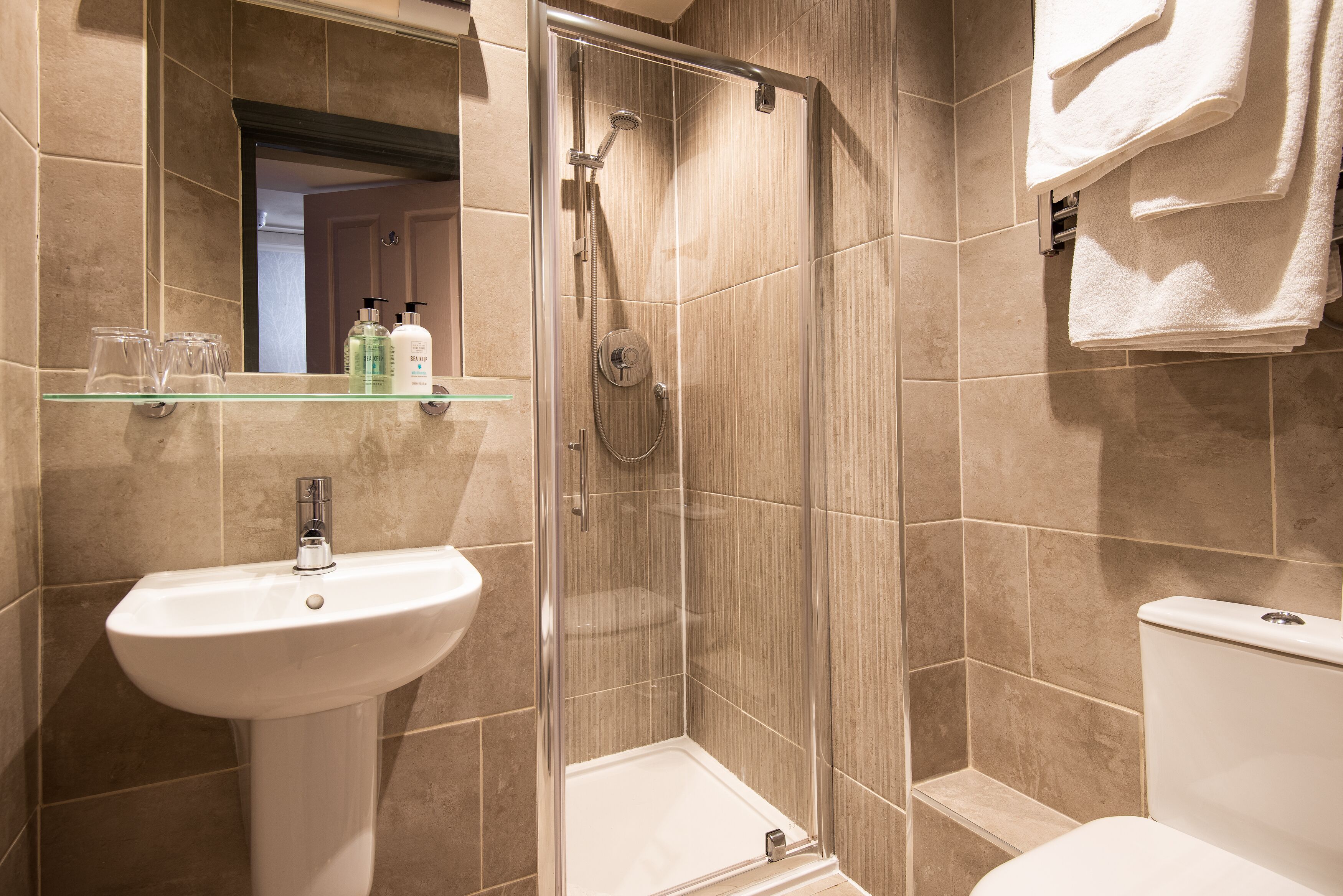 A bathroom with a glass-enclosed shower, a pedestal sink, and a toilet.