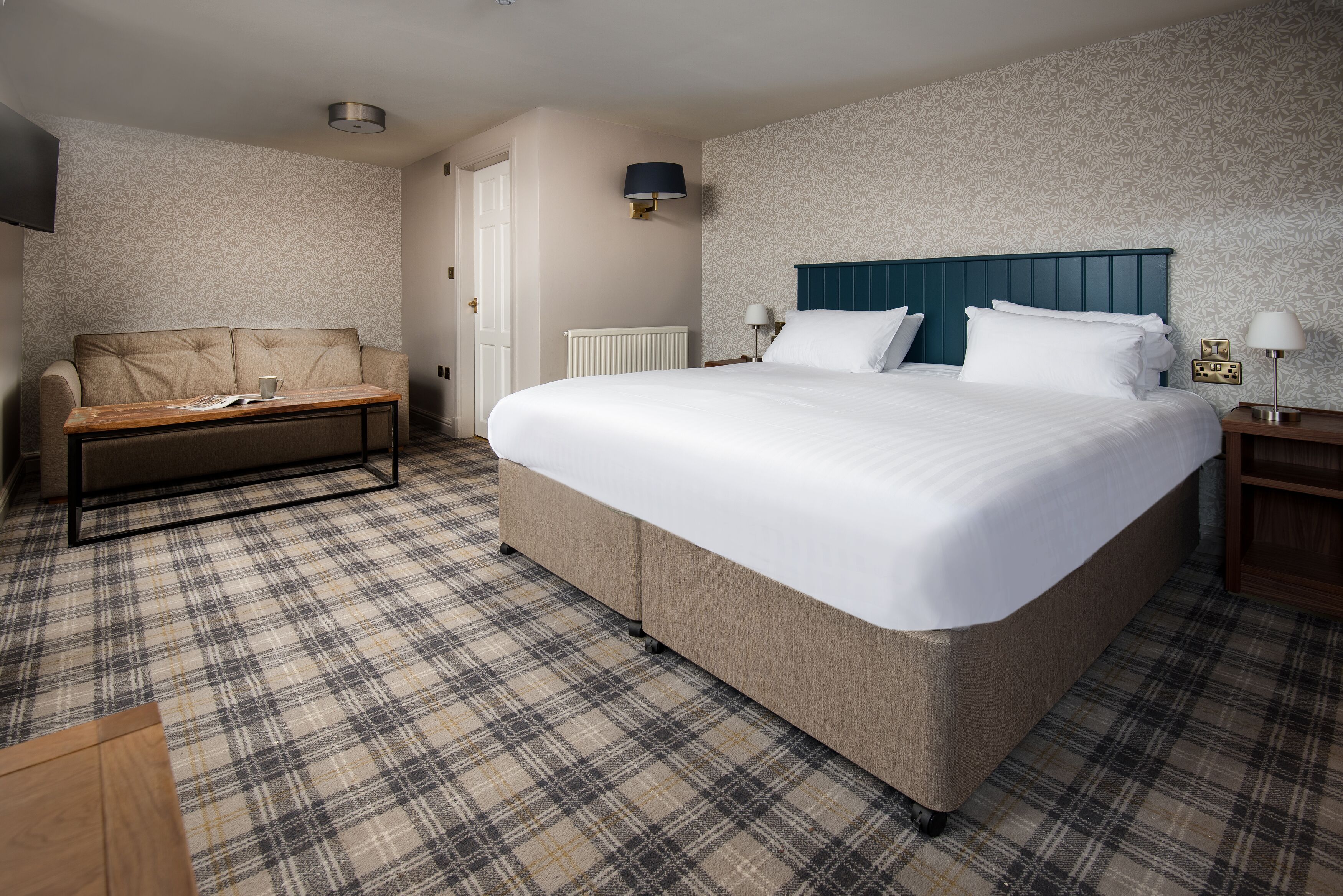 A hotel room with a large bed, a sofa, a small table, and a TV.