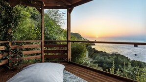 Une terrasse en bois avec un lit et une vue sur la mer au coucher du soleil.