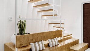 Un escalier moderne avec des marches en bois et des rampes blanches, menant à un banc en bois agrémenté de coussins.