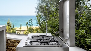 Une cuisine extérieure équipée d’une cuisinière à gaz et d’un évier, avec vue sur une plage et l’océan.