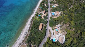 Vue aérienne d’une propriété côtière comprenant plusieurs maisons, une route et une plage.