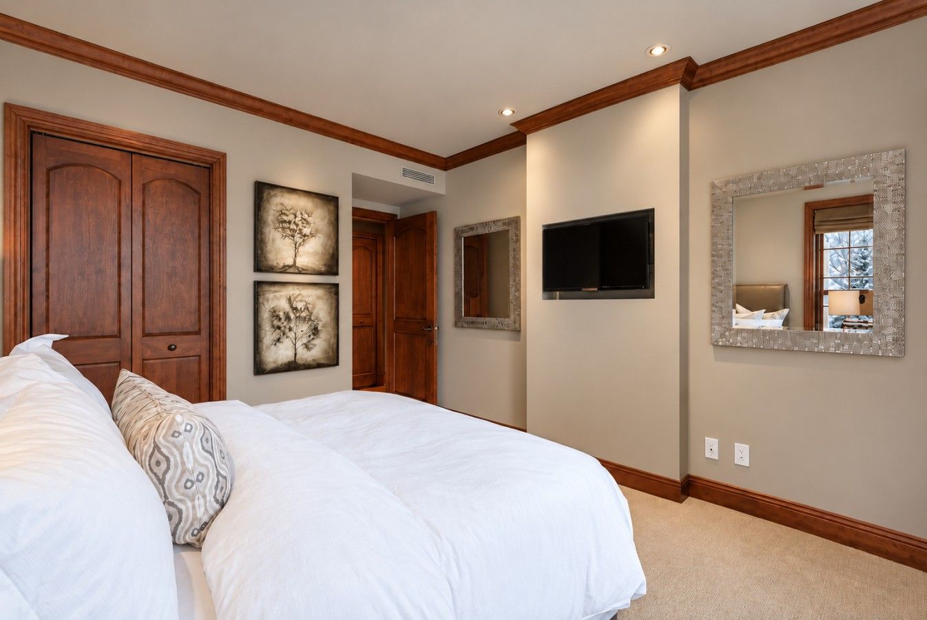 A bedroom with a large bed, wooden wardrobe, artwork, a television, and a mirror.