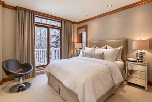 A bedroom with a large bed, a bedside table, a chair, and a window with curtains.