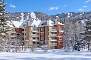 A multi-story hotel with balconies, set against a snowy mountain backdrop.